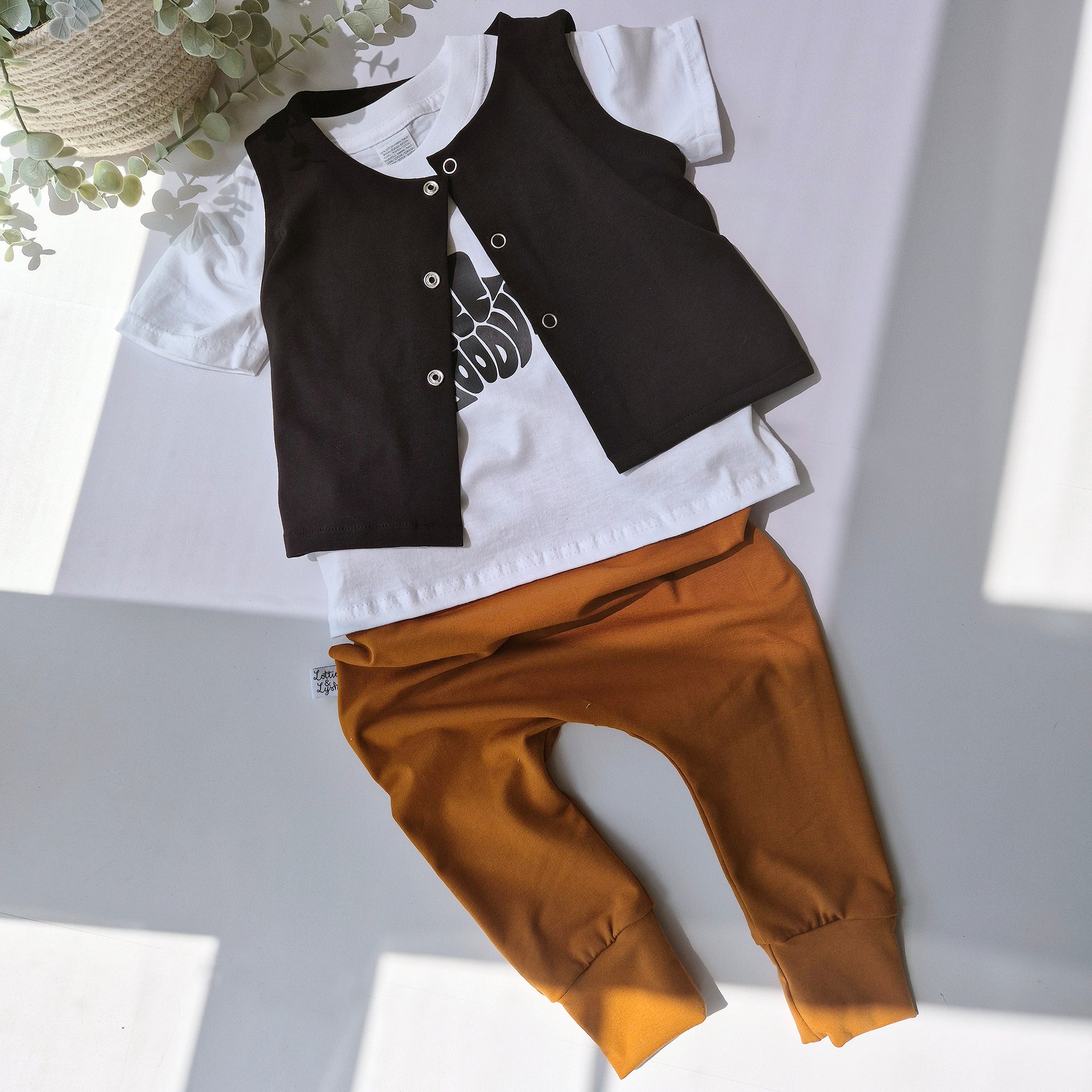 Children's outfit with black and white top and brown pants on a light gray background