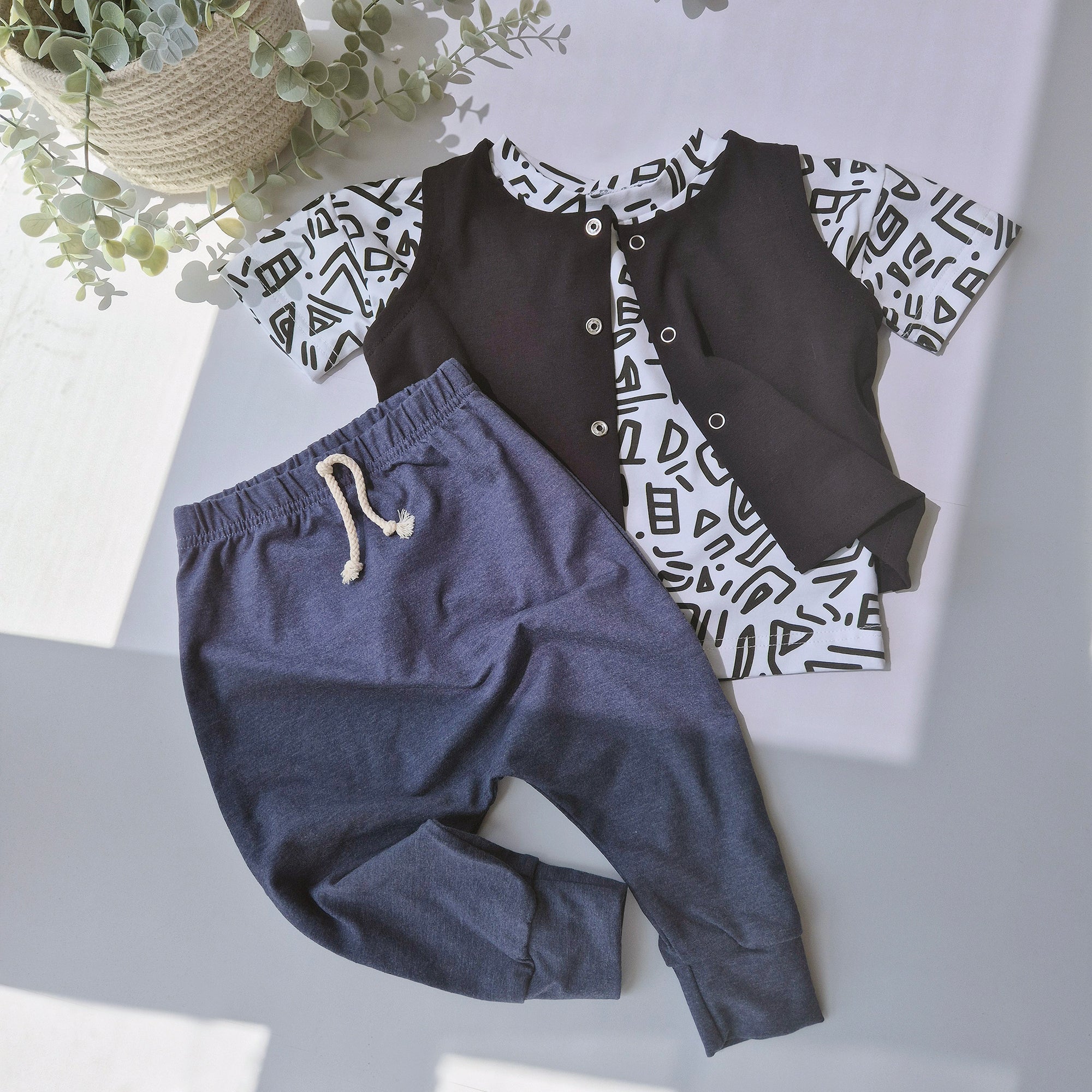 Children's outfit with navy pants and black patterned shirt on a light gray surface.
