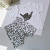 White t-shirt with black graphic design and matching shorts on a light gray background