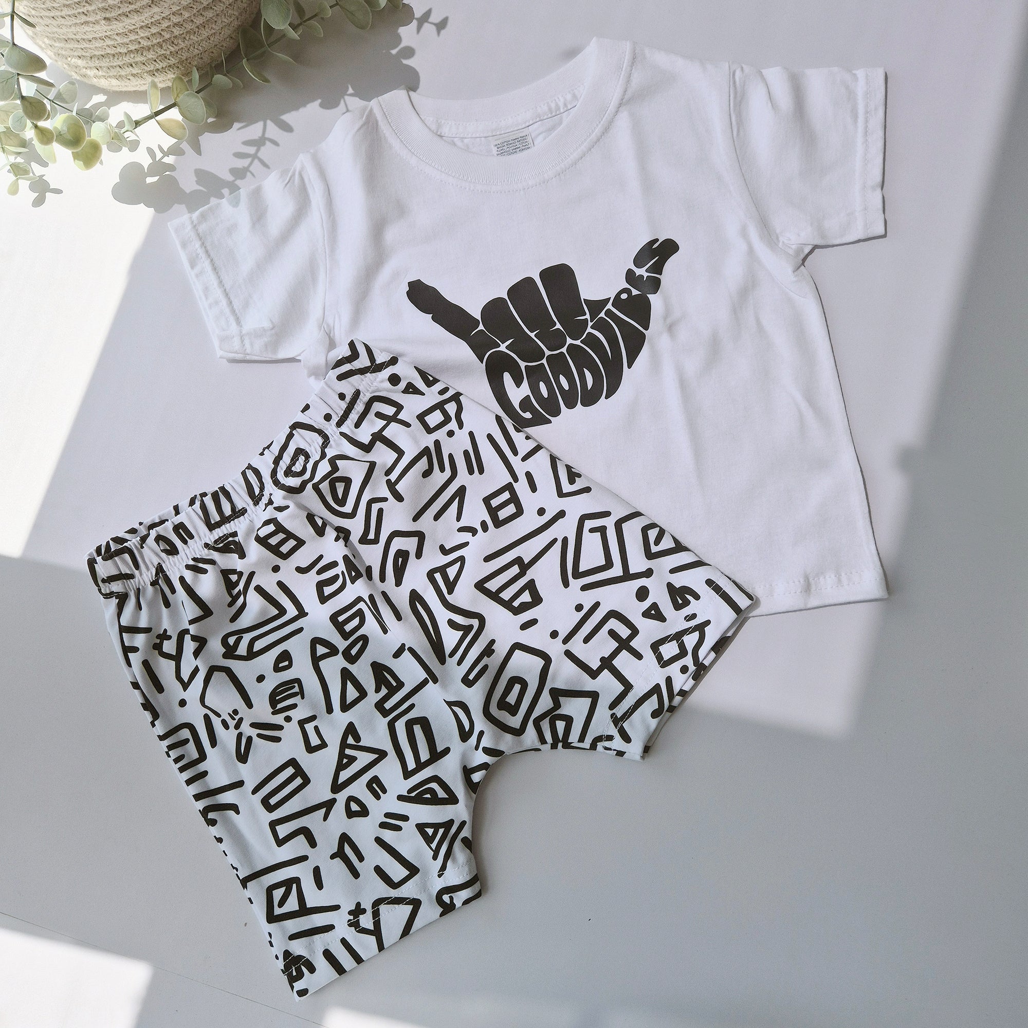 White t-shirt with black graphic design and matching shorts on a light gray background