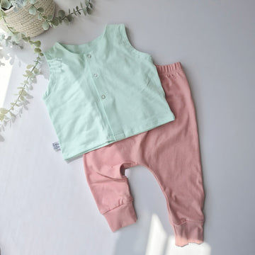 Light green top and pink pants on a light gray background with a plant.