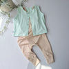 Light green vest and beige pants on a light gray background with a plant.
