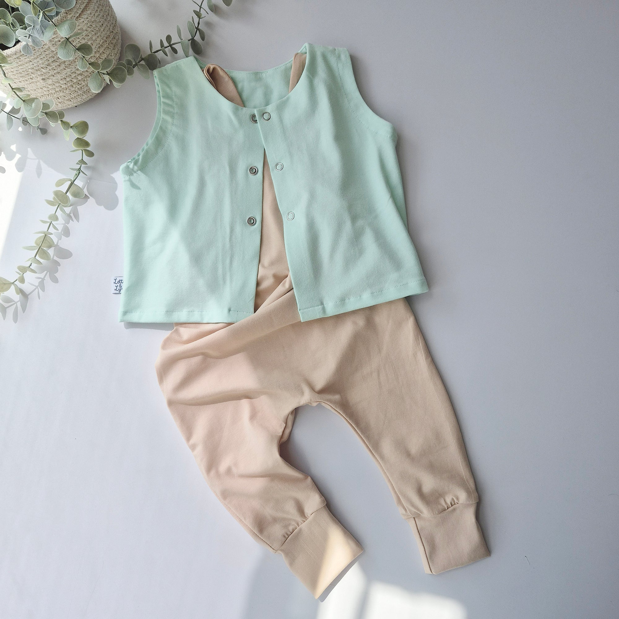 Light green vest and beige pants on a light gray background with a plant.