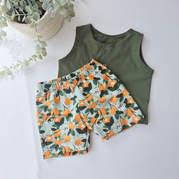 Green sleeveless top and orange print shorts on a white background with a plant.