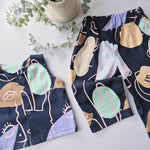 Patterned pants and top on a light surface with greenery in the background