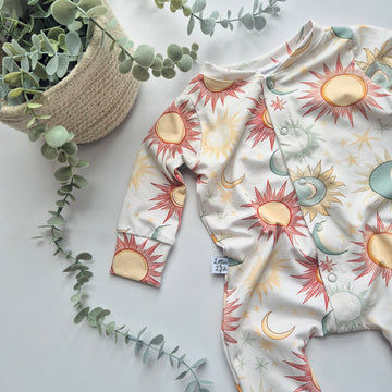 Baby onesie with sun and moon pattern on a light surface with greenery