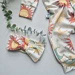 Fabric with sun and moon patterns on a gray surface with green leaves.