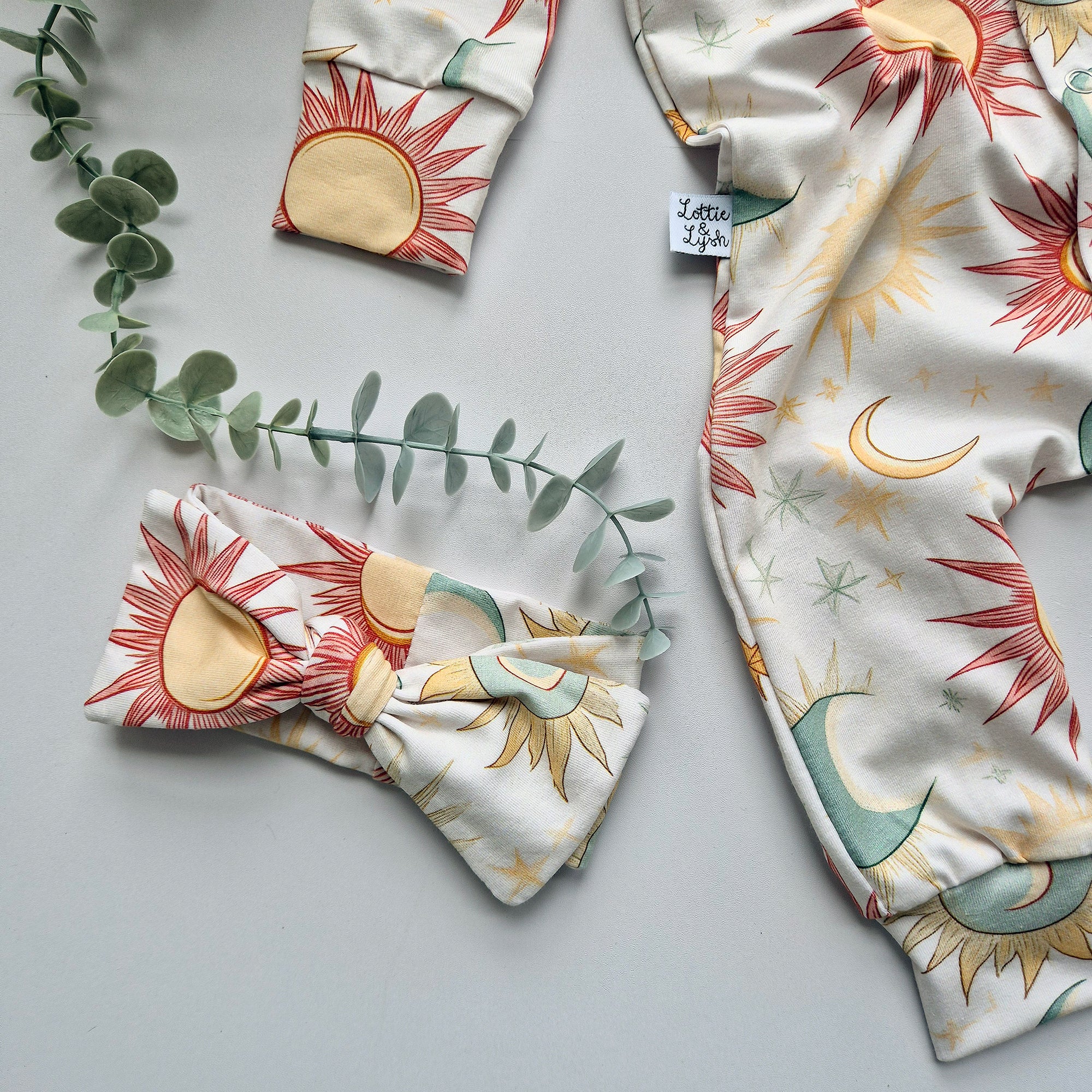 Fabric with sun and moon patterns on a gray surface with green leaves.