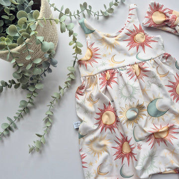 Baby outfit with sun and moon pattern on a light surface with greenery