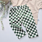 Green and white checkered pants on a light gray surface with a beige top and plant in the background.
