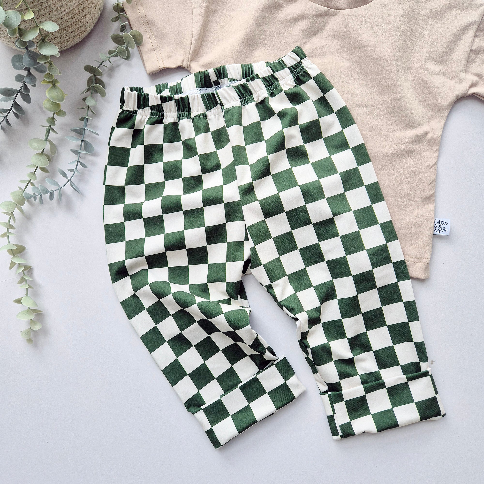 Green and white checkered pants on a light gray surface with a beige top and plant in the background.