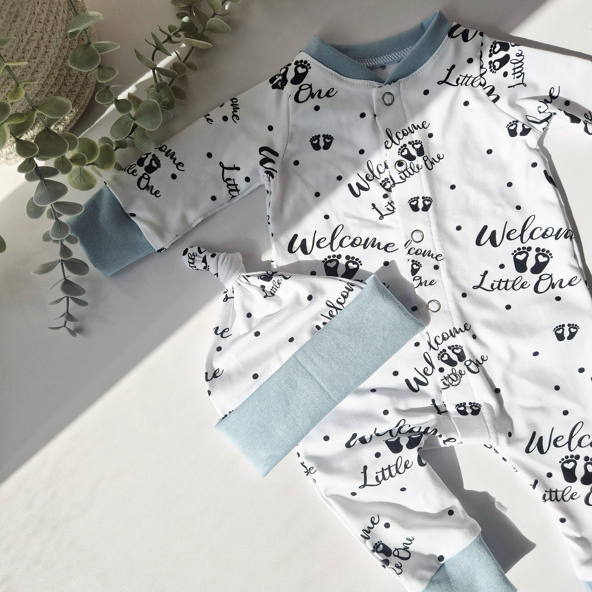 Baby outfit with 'Welcome Little One' text and paw prints on a light background