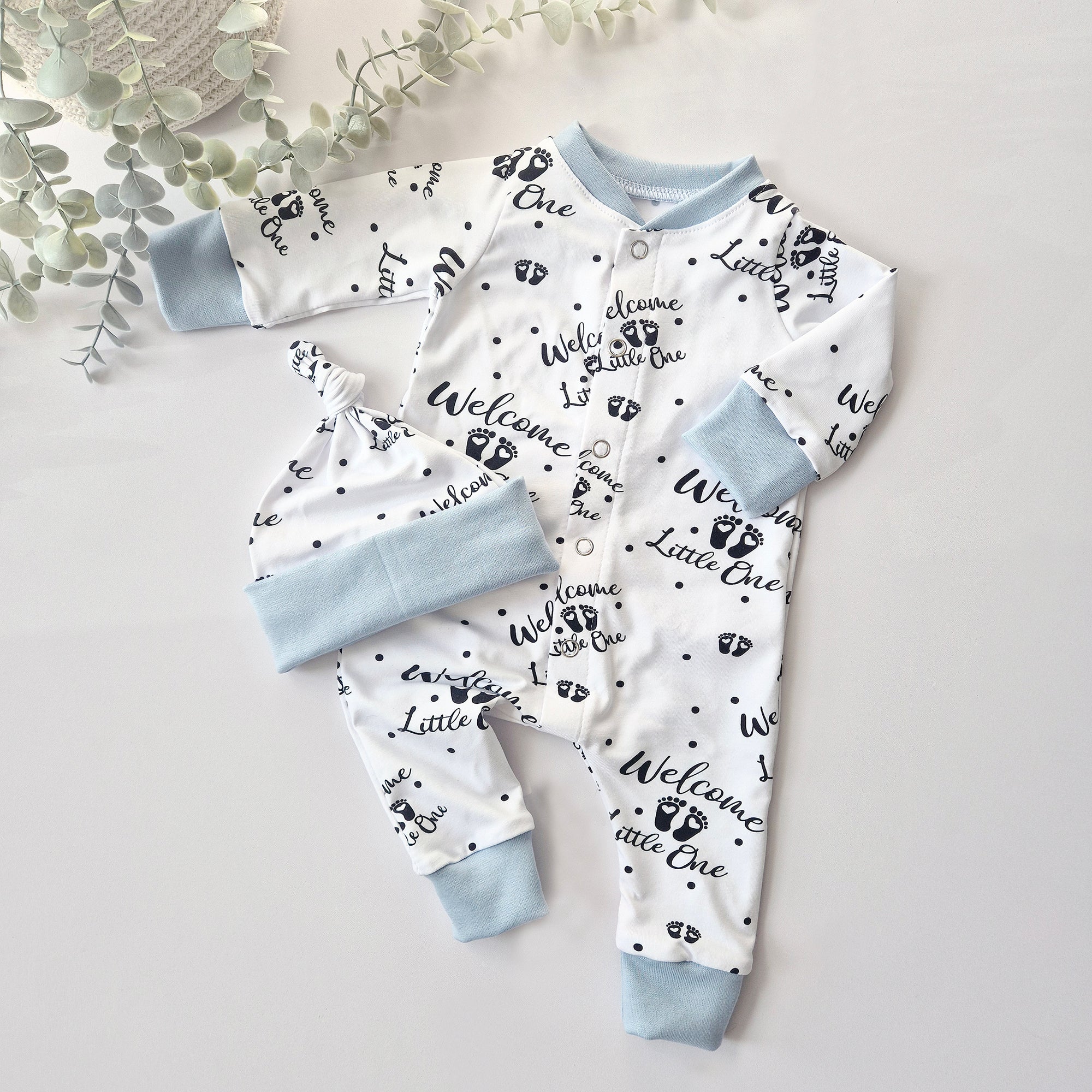 Baby outfit set with white onesie and hat with text and footprints on a light gray background.