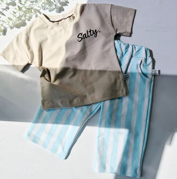 Children's outfit with a t-shirt and striped pants on a light gray surface.