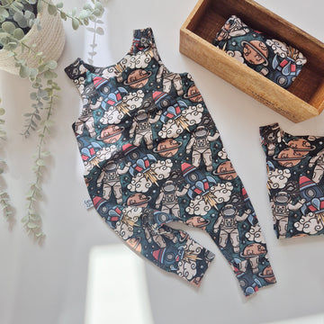Children's romper with astronaut pattern on a white surface with a wooden box and plant.