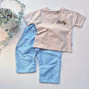 Children's outfit with beige t-shirt and denim shorts on a light background