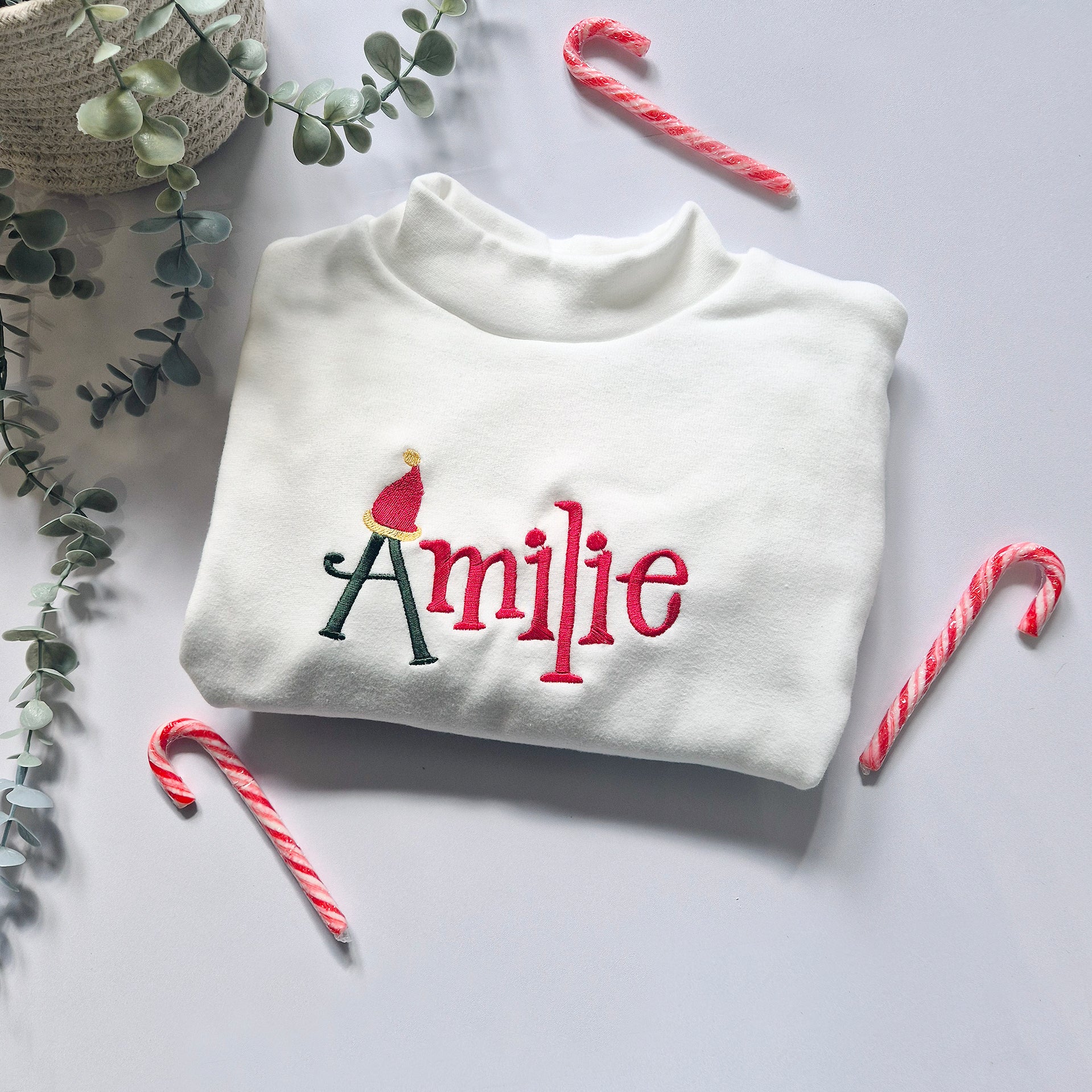 White sweatshirt with 'personalised' embroidery surrounded by candy canes and eucalyptus leaves on a light background