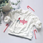 White sweatshirt with 'personalised' embroidery on it, surrounded by candy canes and greenery on a light background