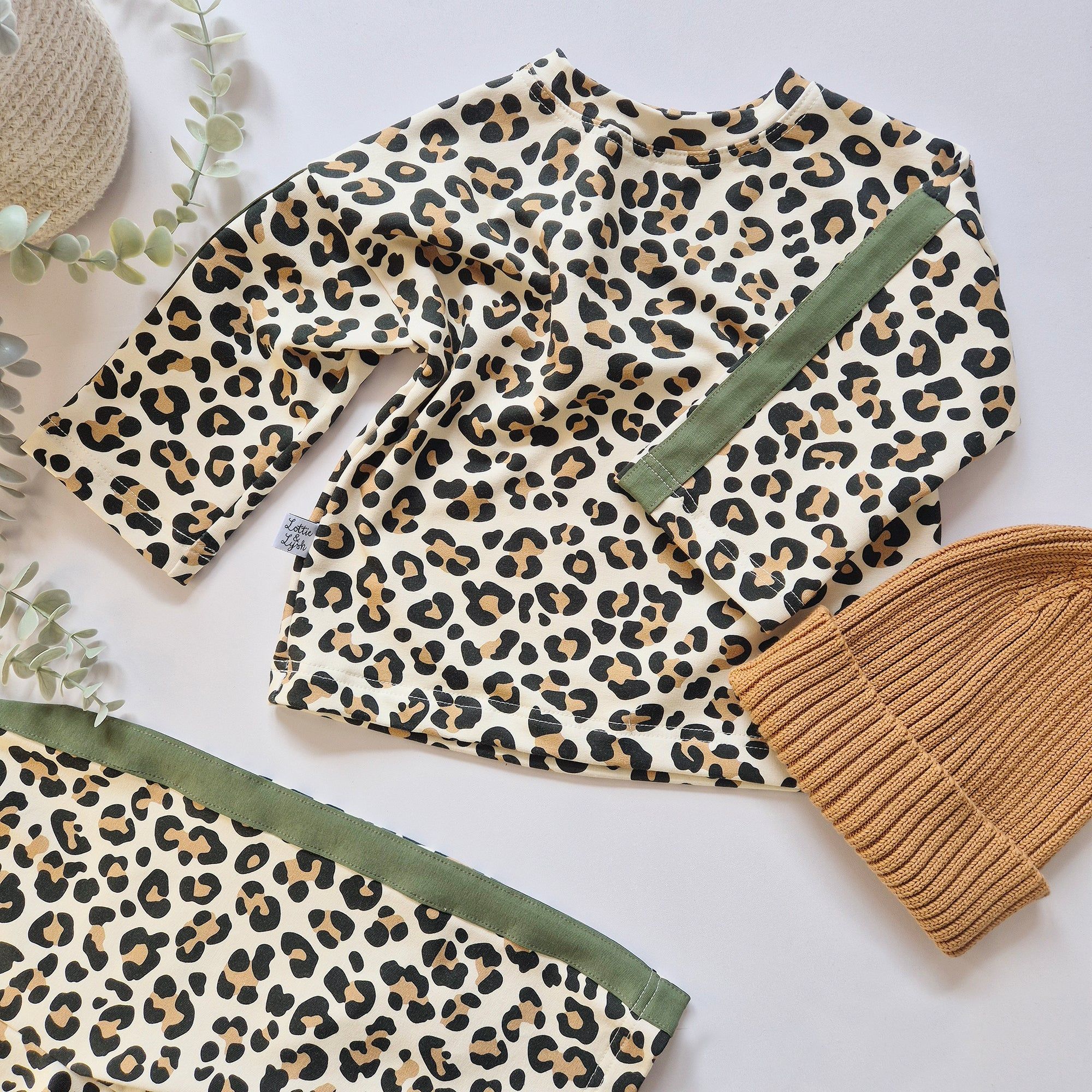 Leopard print outfit with green trim and a brown beanie on a light background