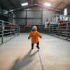 Child in an orange raincoat walking inside a large industrial building with machinery.