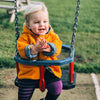 Child in an orange coat on a swing set with a grassy background