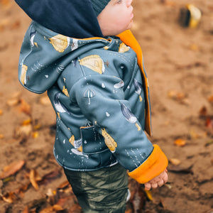 Child wearing a blue jacket with yellow accents and a hood, standing on a dirt path with autumn leaves.