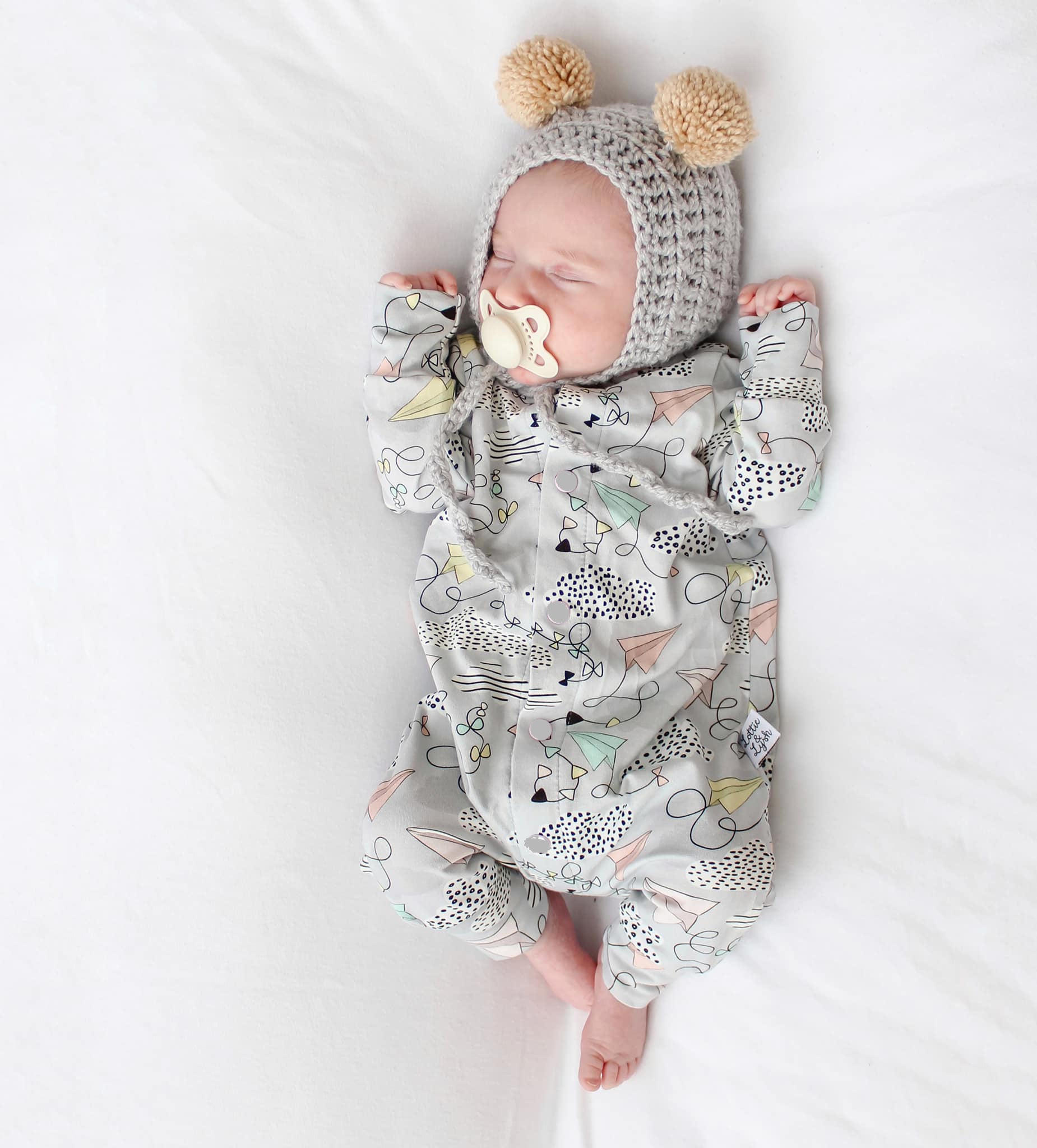 Newborn baby in a patterned outfit and knitted hat with pom-poms on a white background
