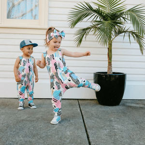 Two children in colorful outfits standing outdoors next to a potted plant.