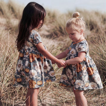 Two young girls in matching floral dresses standing in a field.