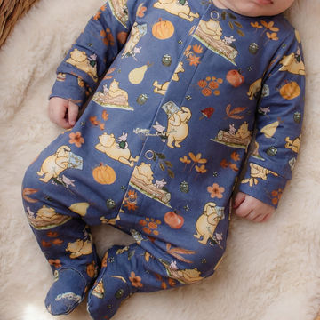 Baby wearing a blue onesie with winnie the pooh character print on a soft surface