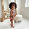 Child wearing a pink leopard print outfit standing in a bright room with a mirror and stool.