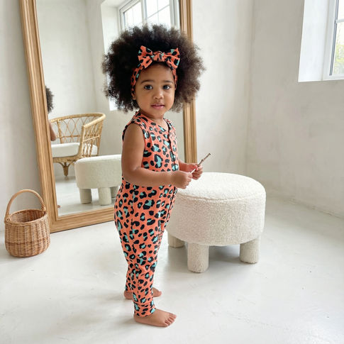 Child wearing a pink leopard print outfit standing in a bright room with a mirror and stool.