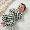 Cool baby clothes - Forest green and cream check skate inspired baby romper by Lottie & Lysh worn by an 8 month old baby boy with dark and hair blue eyes. Lying on a white background alongside a beige knitted blanket.