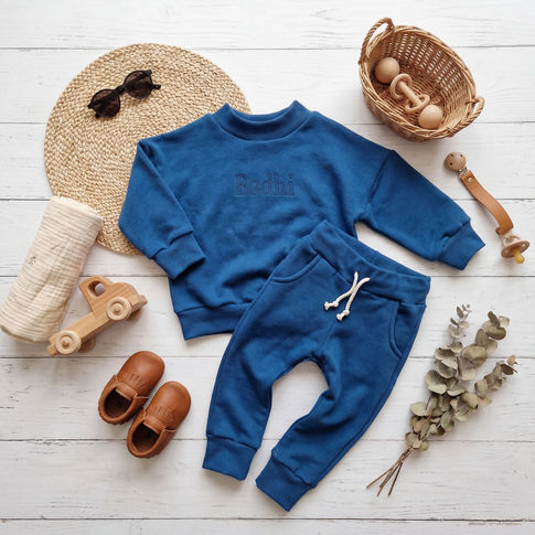 Blue children's personalised sweatshirt and pants set on a wooden surface with toys and a basket.