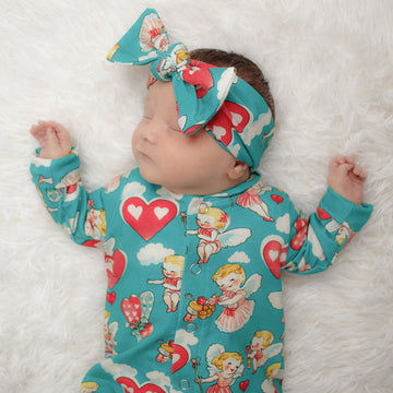 Sweet sleeping newborn baby girl wearing a cherubs printed baby romper with matching bow headband