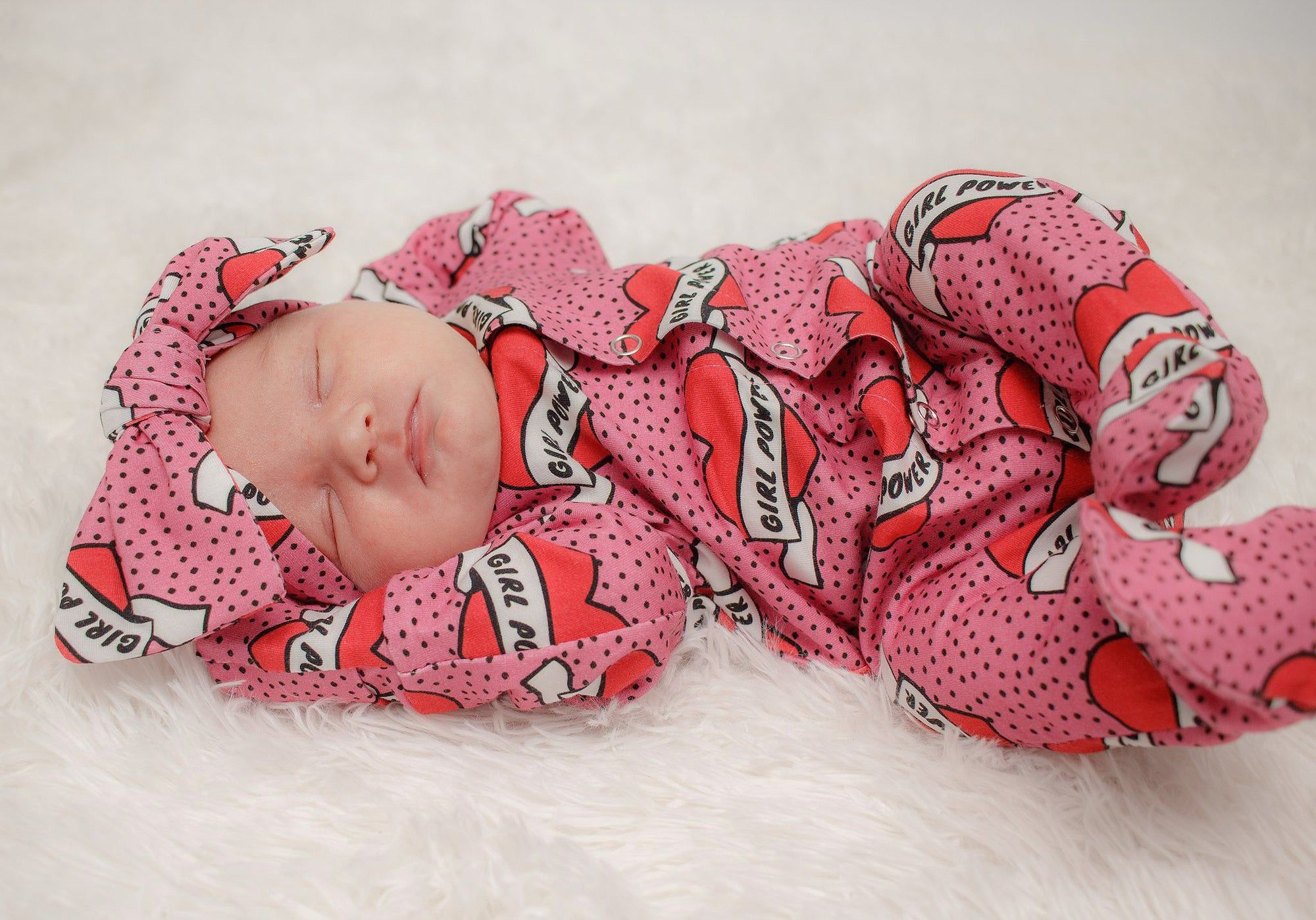 Pink baby girl babygrow with integrated mitts and feet. Worn by a sleeping newborn baby girl with a matching headband.
