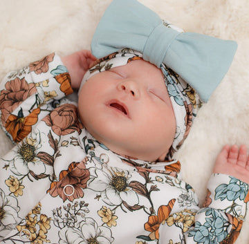 sleeping newborn baby girl wearing a floral turban headwrap with blue bow, and a matching floral babygrow . Outfit ethically produced by Lottie & Lysh
