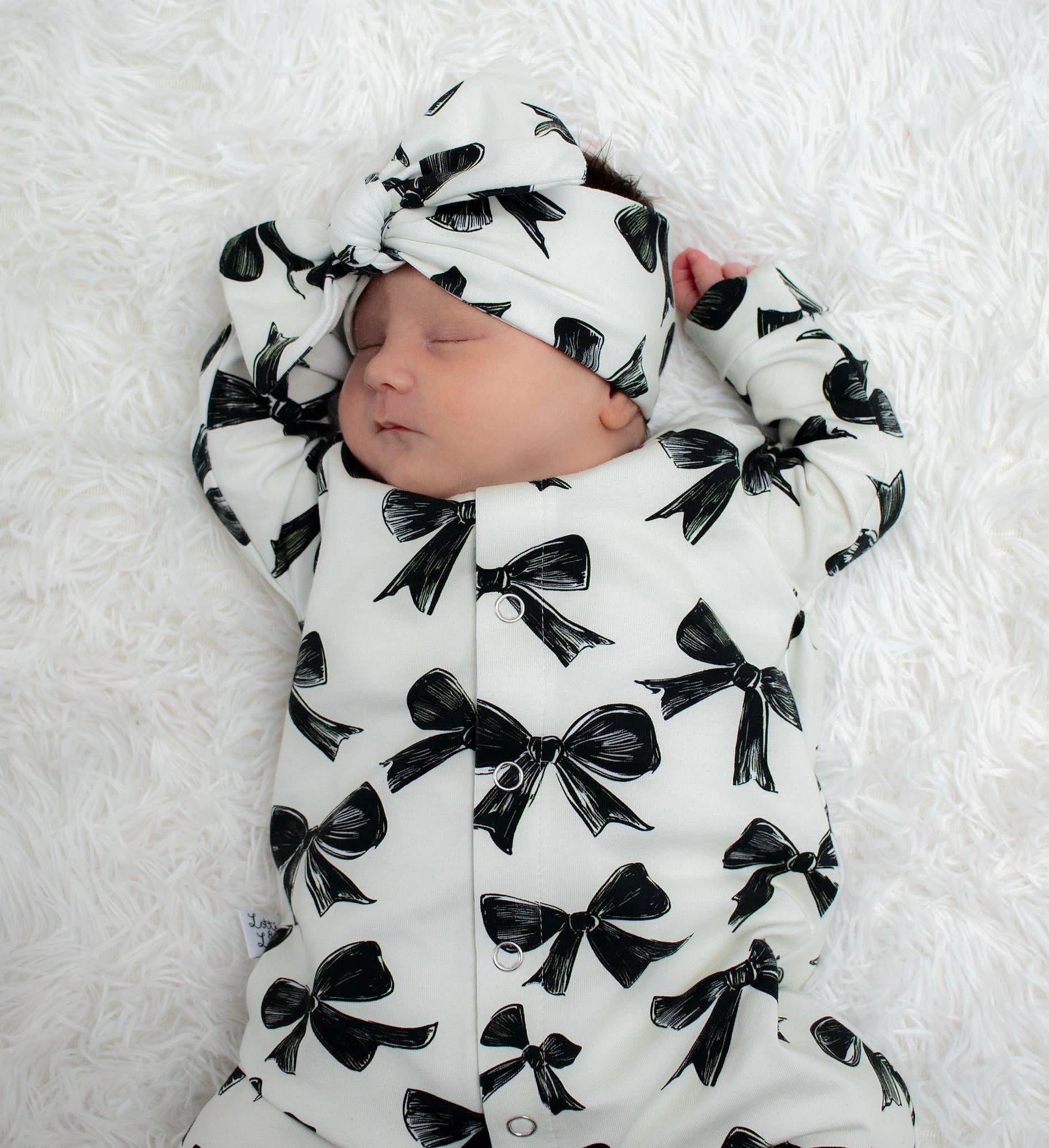 New baby girl wearing a bow print babygrow with coordinating headband. Ethically and sustainably created by Lottie & Lysh in Cornwall.