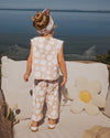 Child in a floral outfit standing on a sunlit deck with ocean view