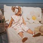 Child sitting on a couch with floral patterns, surrounded by decorative pillows and a hat.