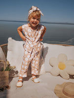 Child in a floral outfit standing on a beach with ocean view