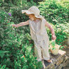 Child in a garden wearing a sun hat and striped outfit, holding a basket.
