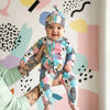 Baby in a colorful outfit with abstract patterns, held by a person against a patterned background.