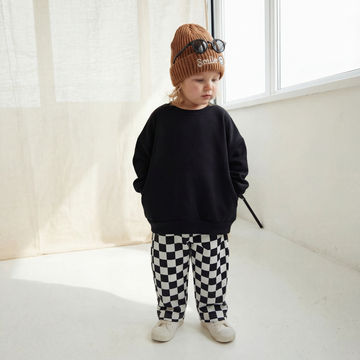 Child wearing a black sweatshirt, checkered pants, and a brown knit hat with sunglasses on a white floor.