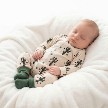 sleeping baby biy wearing beige and leopard print cactus romper with dark green socks.