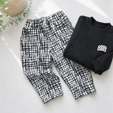 Black and white checkered pants and a black sweatshirt with 'Good Vibes' text on a light surface.