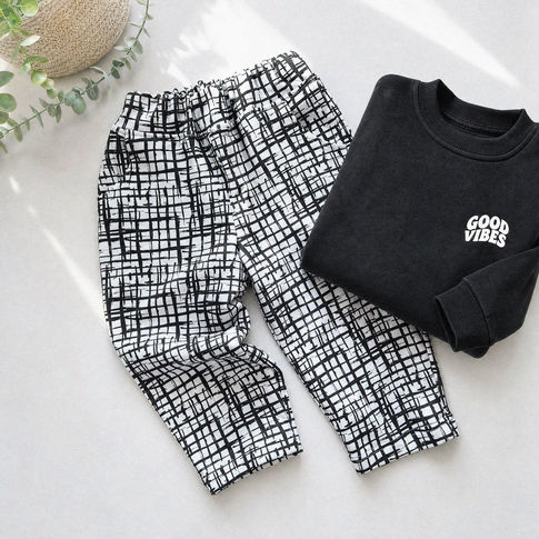 Black and white checkered pants and a black sweatshirt with 'Good Vibes' text on a light surface.