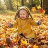 Child in a yellow coat with bunny ears playing in autumn leaves.