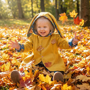 Child in a yellow coat with bunny ears playing in autumn leaves.