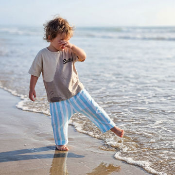 Child playing on a beach wearing a t-shirt with 'Salty' printed on it and blue and white stripey baggy trousers